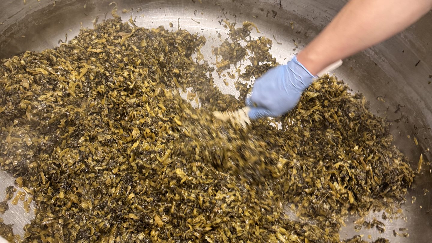 大釜のなかの高菜を手で混ぜているところ